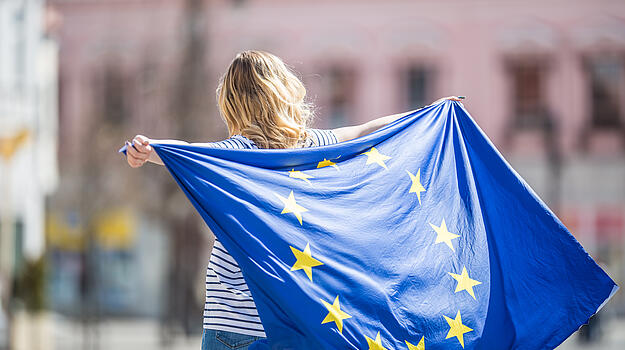 Eine Frau hält eine Europafahne hinter ihrem Rücken nach oben.